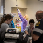 An emergency department nurse prepares an IV for the arriving patient and EMS provides the trauma team with the patient injury report.