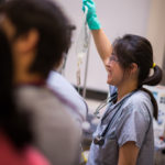 An emergency department resident holds the patient’s IV, preparing for transfer out of the trauma suite.