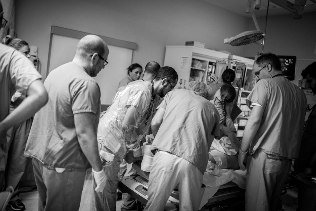Dr. Sne, Trauma Team Leader, stands at the foot of the bed guiding the team members through a systematic process of examining the patient.