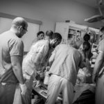 Dr. Sne, Trauma Team Leader, stands at the foot of the bed guiding the team members through a systematic process of examining the patient.