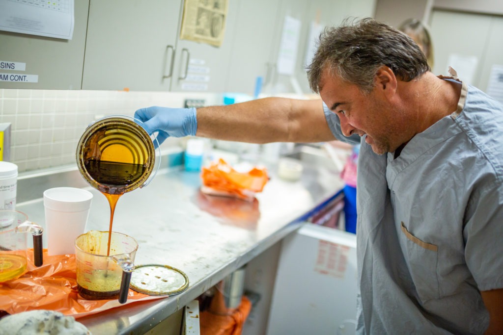 Mould Room Technician pouring liquid substance into measuring cup to prepare expandable foam leg cradle