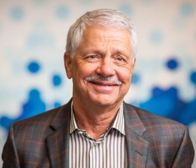 Headshot of Dr. Barry Lumb, a man with a grey moustache wearing a grey striped shirt and suit jacket