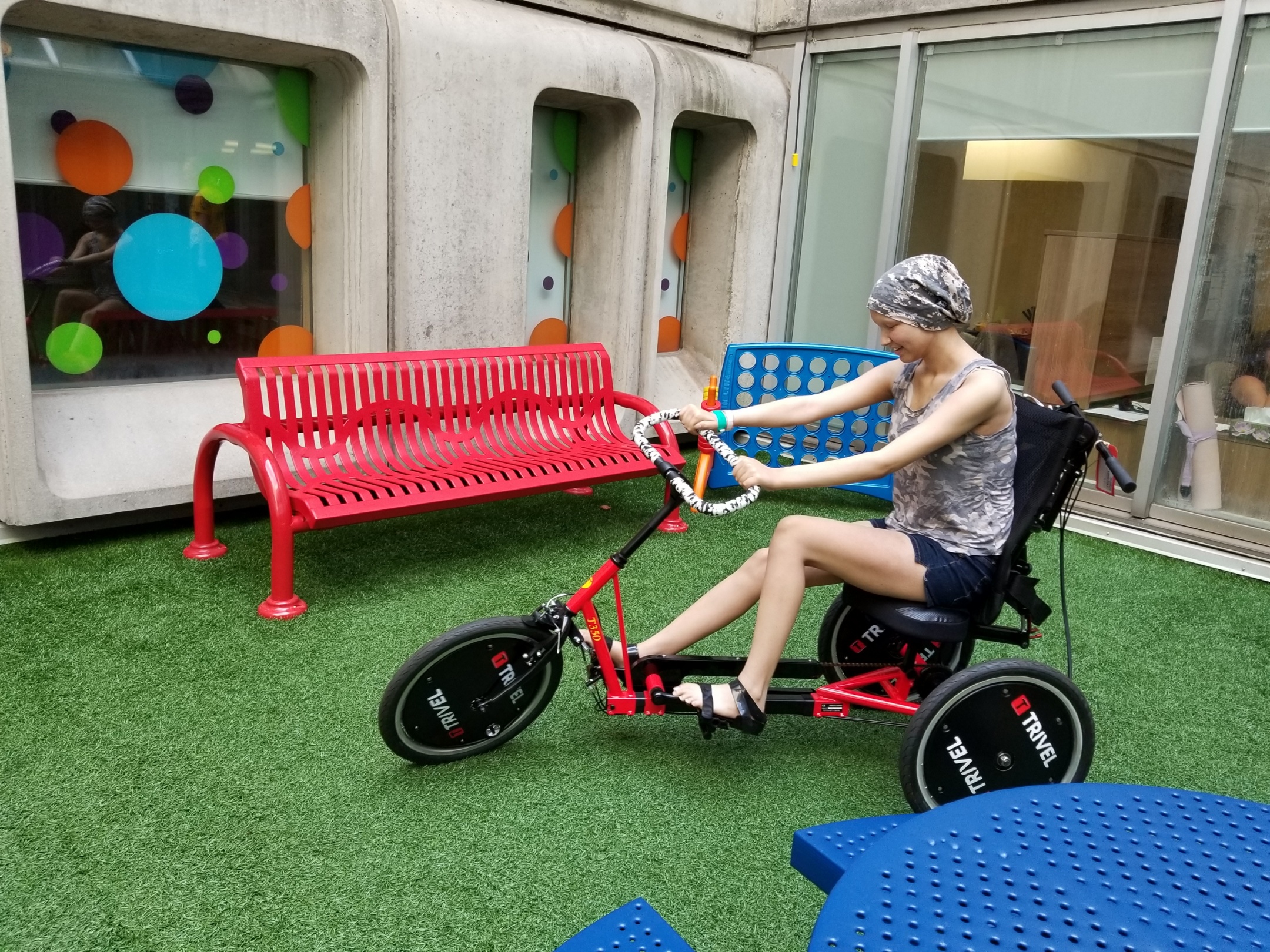 Sky rides an adaptive tricycle in a courtyard at McMaster Children's Hospital