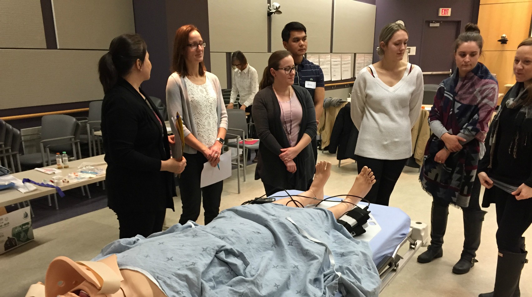 Health care staff listen to a leader teaching a lesson over a simulation mannequin