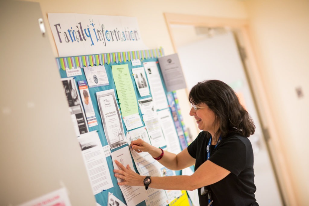 A palliative care social worker posts a flyer to a hospital information board.