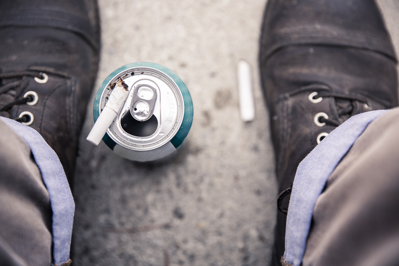 Two male feet surround an empty beer can with a cigarette on top