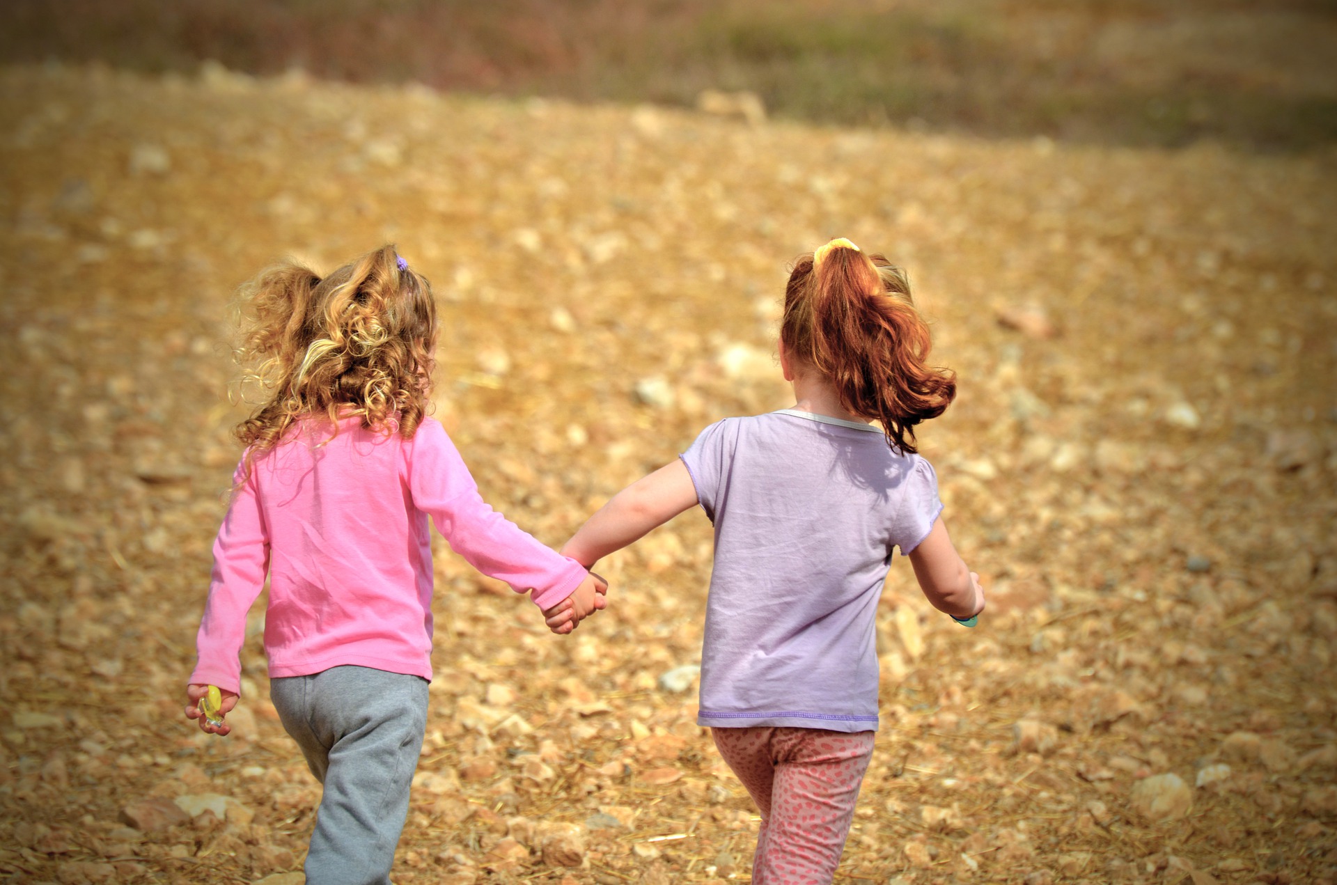 two little girls running in a field holding hands