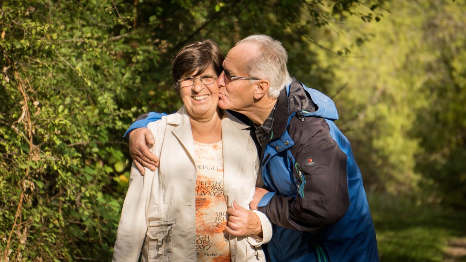 an older man kissing his wife on the cheek while they walk outside