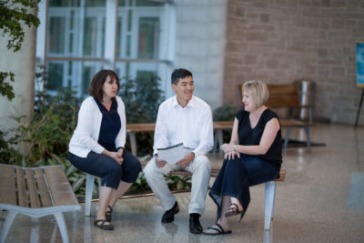 patient advisor, Martha Winhall, Dr. John You, and Marilyn Swinton sit on a bench talking in a brightly lit atrium