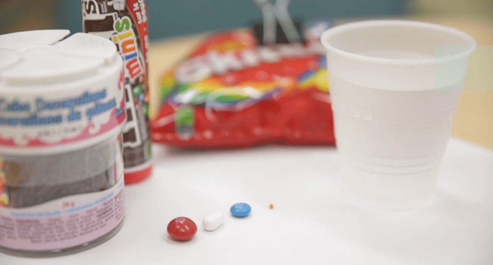 candy of different sizes on a desk top including a skilttle, a tic tac and a sprinkle