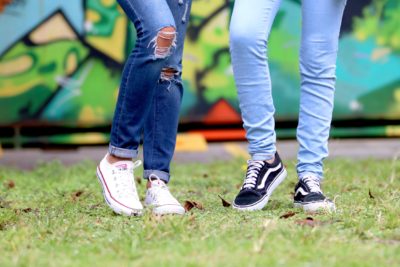 The legs of two teenage girls in jeans and sneakers, standing on grass