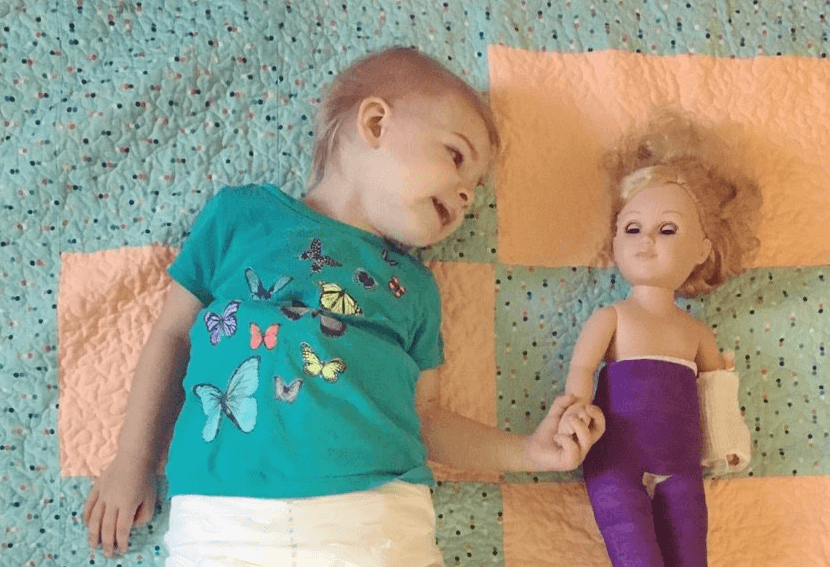 Madison in a purple cast holding her doll's hand
