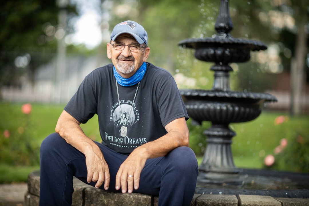 A man wearing a ball cap sits in a park by a fountain