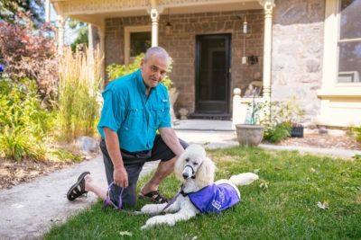 A man sits in front of a house with a service dog he is caring for