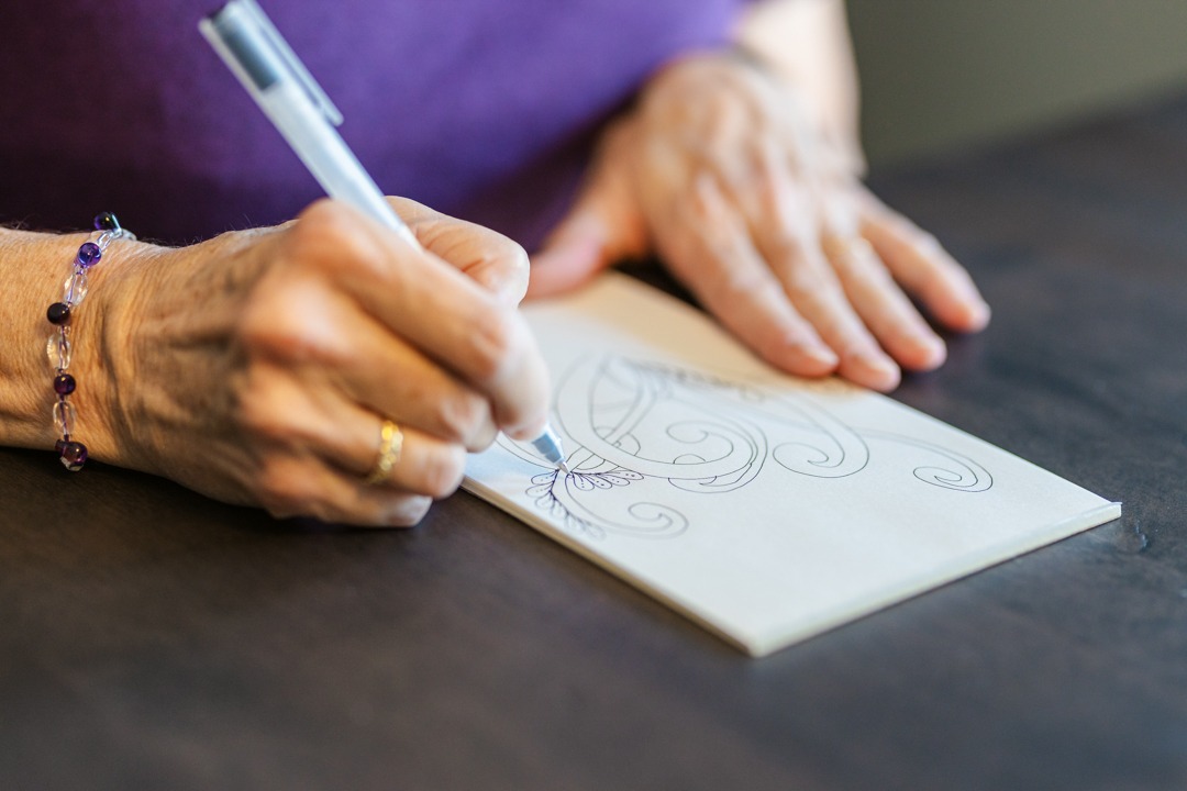 A person's hand is drawing intricate line drawings on a piece of paper