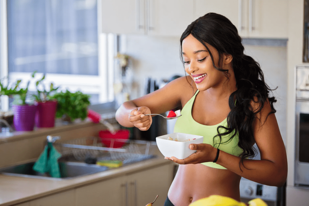 A woman eats a bowl of fruit in her kitchen