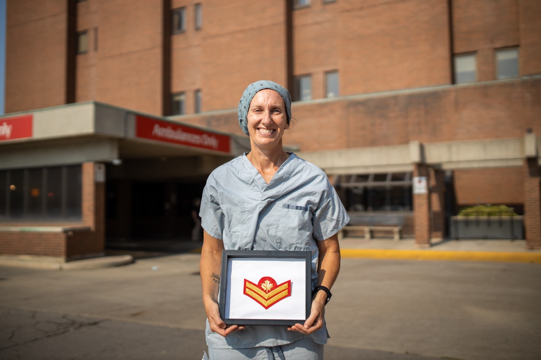 Nurse dressed in hospital scrubs, holding badge that represents her military promotion