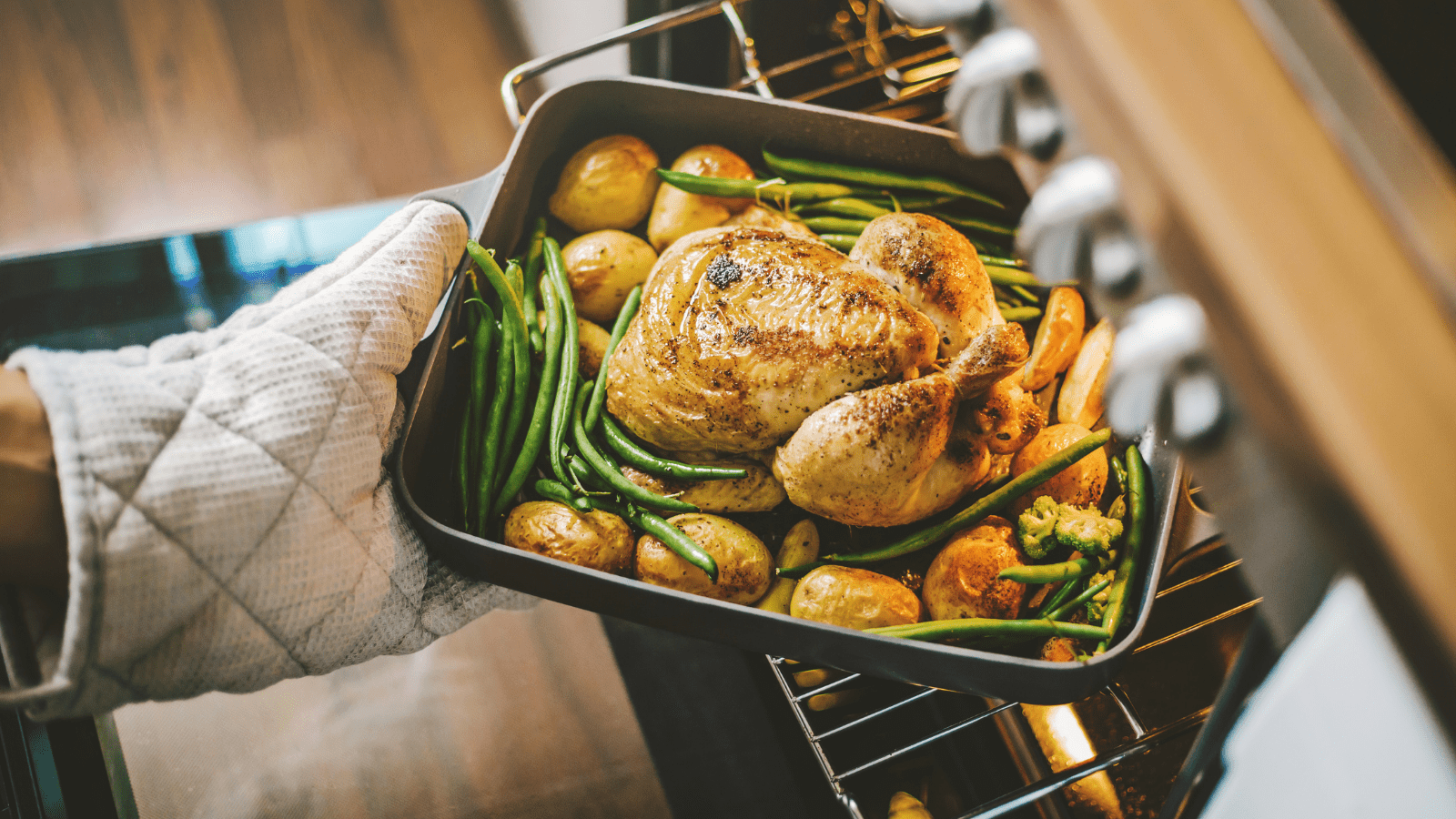 Person removes roasted poultry and veggies from oven