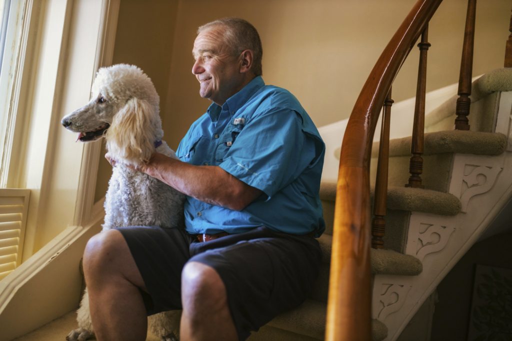 Patient Robb Bendus sitting on the stairs with his dog, both looking out the window