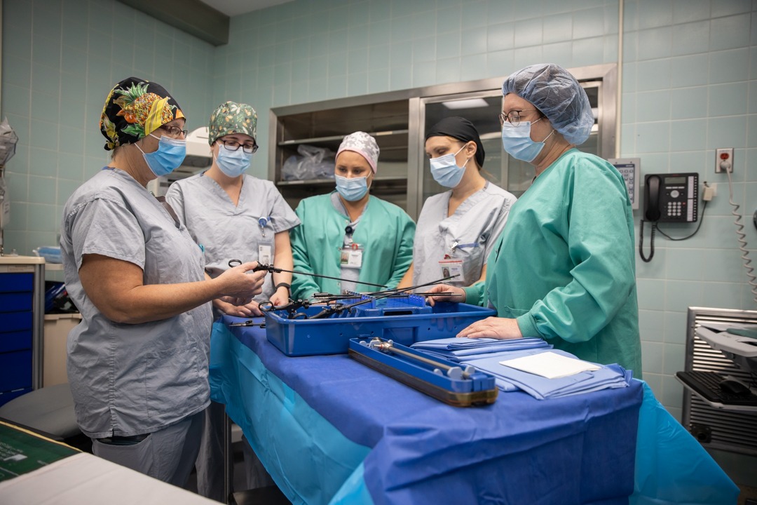 Four registered nurses and a nurse educator inspect equipment on a table in the West Lincoln Hospital new operating room. They are all dressed in scrub gowns, masks and surgical caps.