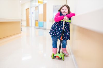 Delilah Myke stands on her bright green scooter in the hallways at McMaster Children's Hospital