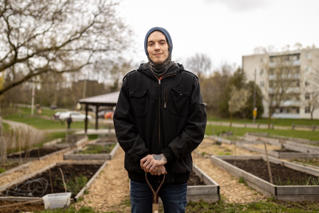 Ryan Duguay stands in the community garden wearing a hooded sweater and black jacket