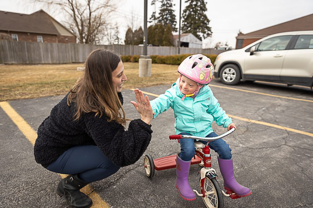 A child riding a tricycle gives her mother a high five.