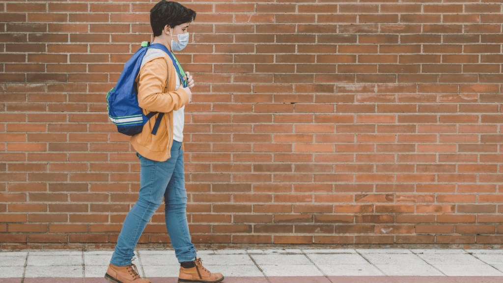 Stock photo of young student wearing face mask walking by a brick wall