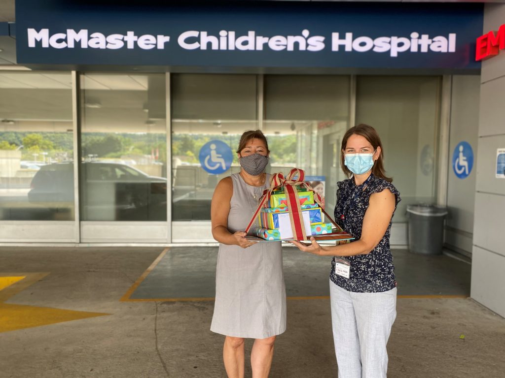 Rose giving a gift basket to Jenny from McMaster Children's Hospital Child Life department outside of the hospital.