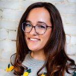 Head shot of Sabrina Mastrangelo, long brown hair, glasses, grey knit sweater with pineapple pattern