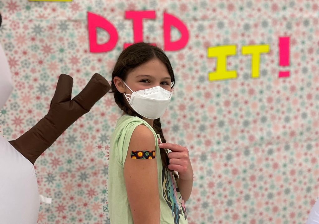 child pointing at a bandaid on her arm where she got her vaccine