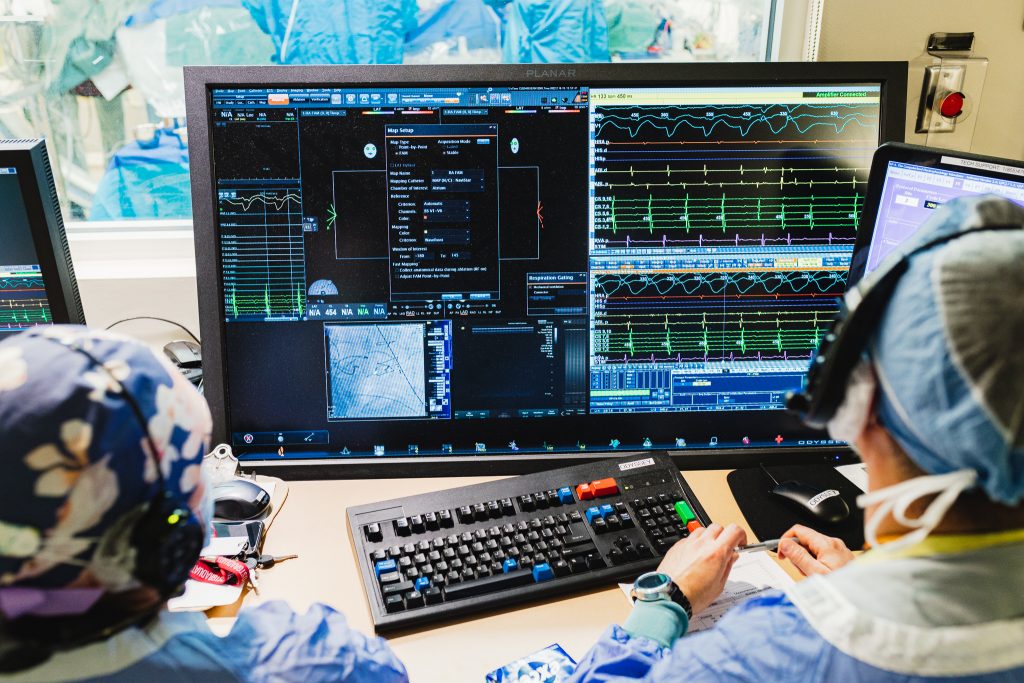 Two health care providers monitor a complex screen full of information during a heart procedure