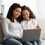 Happy african american mother and kid using laptop together sitting on a couch