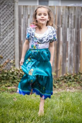 A 4-year-old girl dances in the grass, wearing a blue princess dress