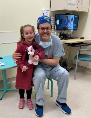 Dr. Luis Braga in scubs with a three-year-old patient in a red dress