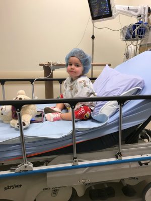 A three-year-old girl sits in a hospital bed after surgery