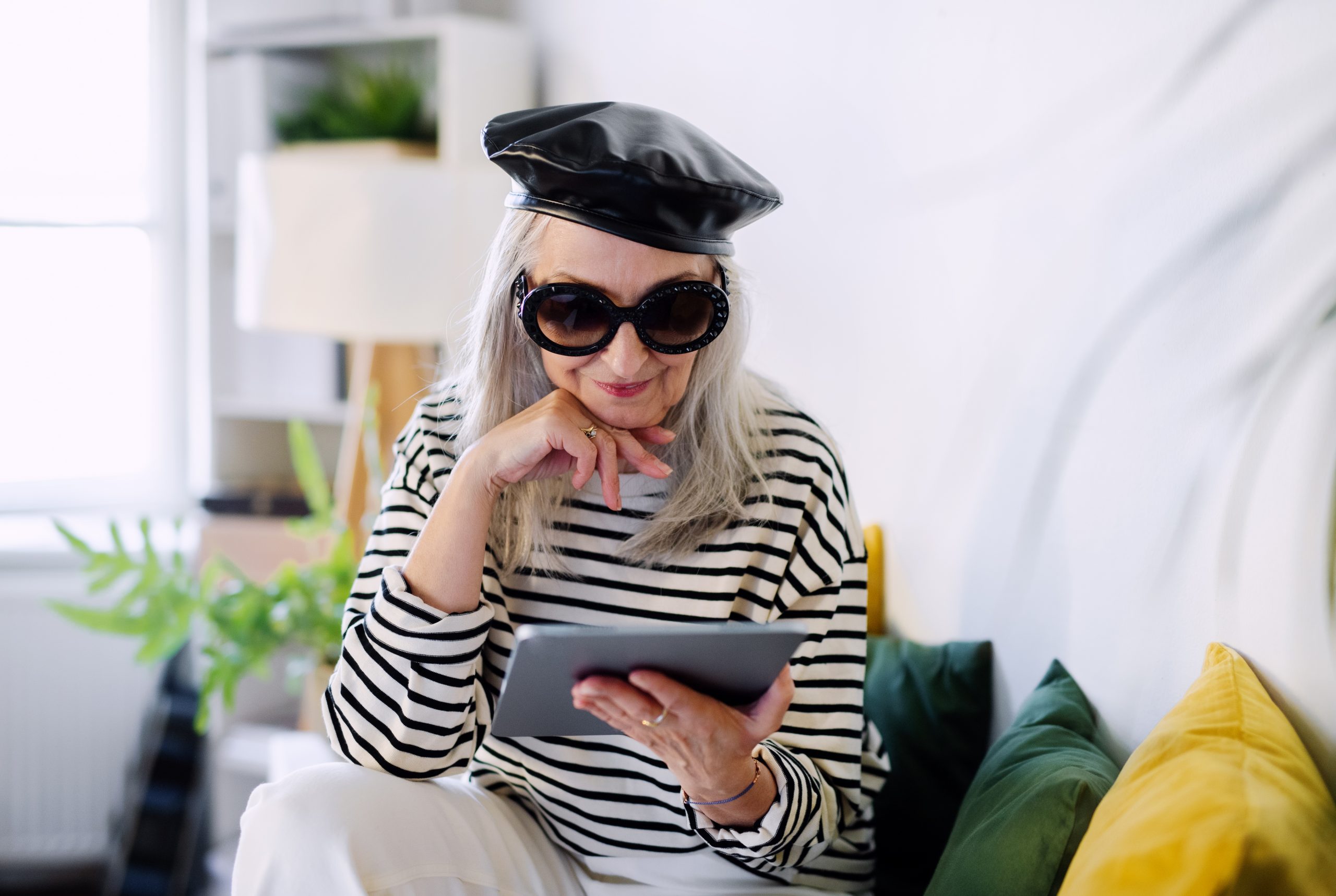 An older adult in a beret and black and white striped shirt looks at her tablet computer