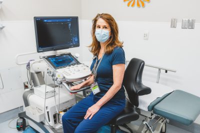 Lisa Neziol, wearing a face mask, sitting beside the new ultrasound machine
