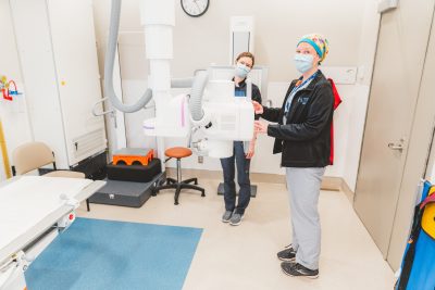 Katie Martin and Jennifer Wiebe wearing face masks and scrubs, standing beside the new X ray machine