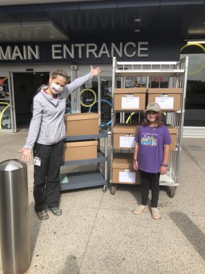 Photo of child life specialist Jenny Cooke with a child and a stack of boxes at the main entrance of McMaster Children's Hospital