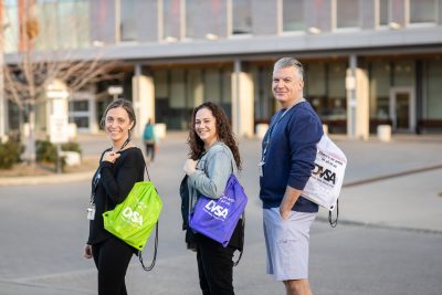 HS staff members Gianna Mazzocato, Miriam Elbard and Peter Neumayer stand outside the Ron Joyce Children's Health Centre wearing backpacks