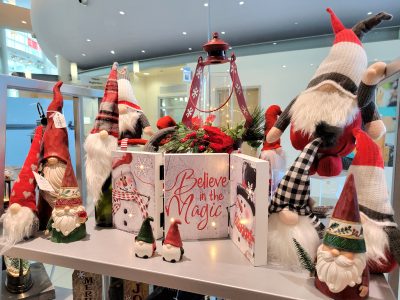 Holiday decor on a table includes a Believe in Magic sign and santa dolls