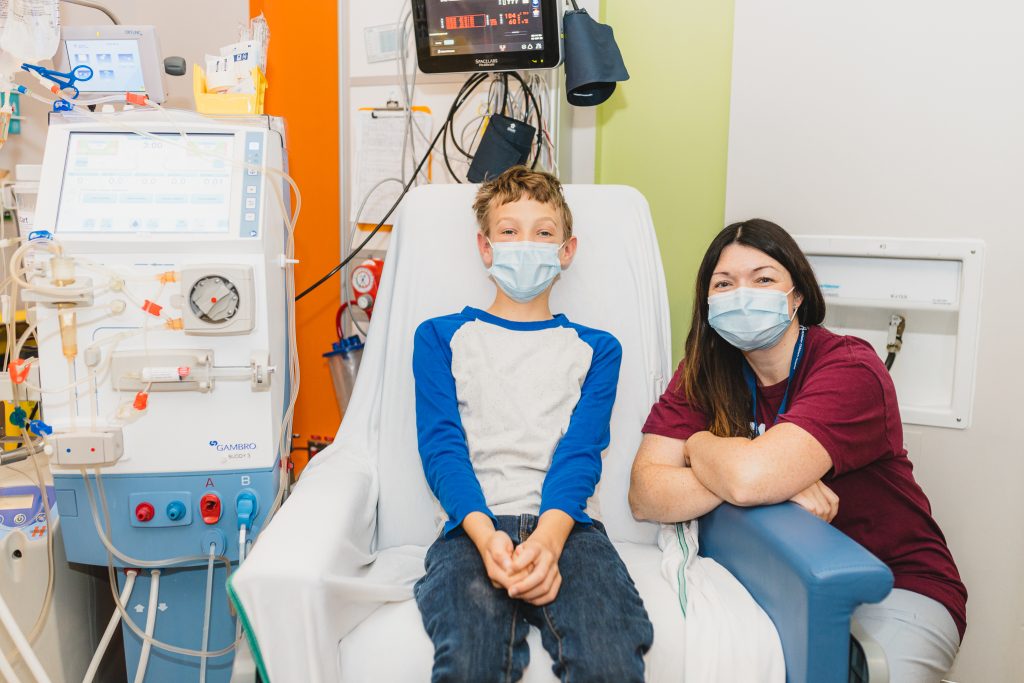 Young kidney transplant patient sitting on hospital chair with hemodialysis nurse beside him.