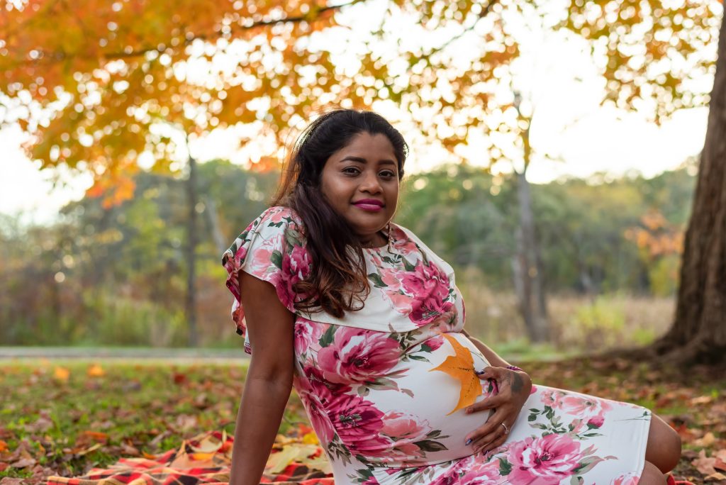 Pregnant woman of South Asian decent sitting under a tree.