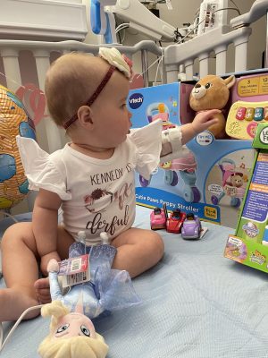 Baby Kennedy sitting in her hospital bed with all her birthday gifts.