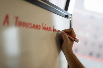 A hand holds a marker, and writes on a whiteboard