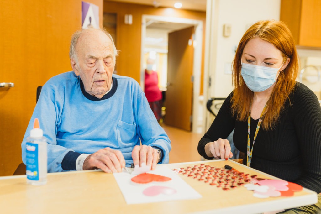 An older man makes a homemade Valentine's Day card with help from a recreation therapist at St. Peter's Hospital