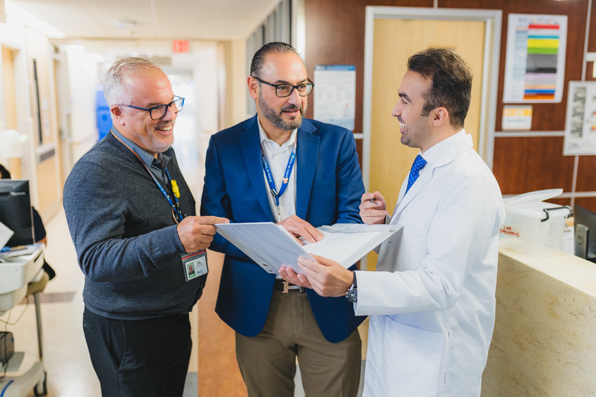 Three men stand in a hospital hallway looking at a file. They are, from left to right, Neil Johnson, HHS' vice president of oncology and Juravinski Hospital site executive, Dr. Khalid Azzam, physician-in-chief at HHS, and Dr. Soltan Abouzobeida.