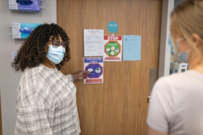 An infection control practitioner at HHS points to signage on a patient's door