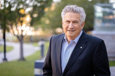 Portrait photo of Dr. Jeff Weitz outside the research building at Hamilton Health Sciences. He is wearing a blue shirt with a dark suit jacket and his order of canada lapel pin.